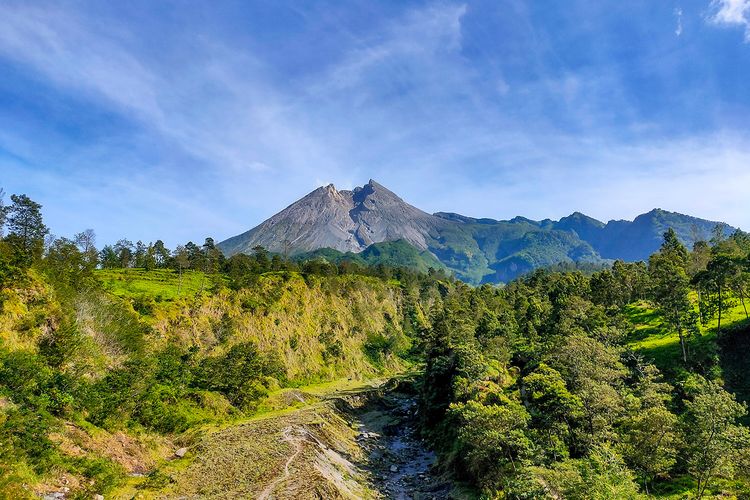 Majestic mountain peak rising over green hills and forest under a clear blue sky.