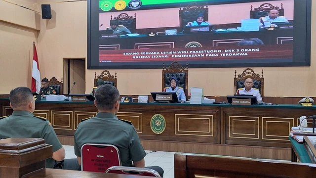Courtroom with three judges at a raised bench, two uniformed men seated in the foreground, and a large monitor showing the hearing.