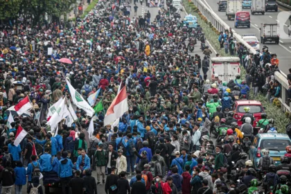 Massive protest on a city highway with hundreds of protesters marching and waving red-and-white flags.