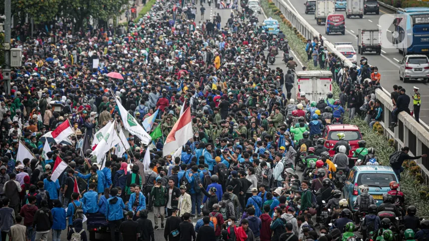 Massive protest on a city highway with hundreds of protesters marching and waving red-and-white flags.