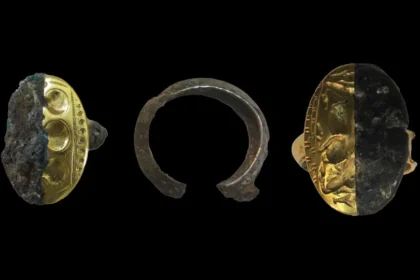 Three archaeological artifacts on a black background: a gold ring with decorative band partly encrusted in dark material, a rusted metal ring fragment in the center, and a gold coin half-buried in dark crust on the right.