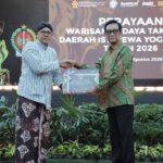 Two men in batik attire shake hands on a stage while presenting a certificate at a cultural heritage event in Yogyakarta, 2026, with a large backdrop behind them.