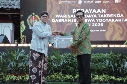 Two men in batik attire shake hands on a stage while presenting a certificate at a cultural heritage event in Yogyakarta, 2026, with a large backdrop behind them.