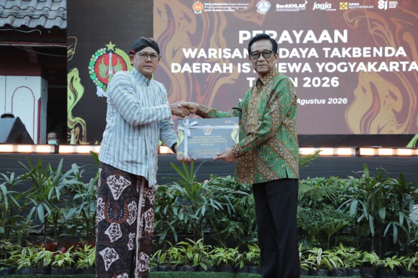 Two men in batik attire shake hands on a stage while presenting a certificate at a cultural heritage event in Yogyakarta, 2026, with a large backdrop behind them.