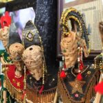 Colorful woven straw puppets with beaded outfits and tassels on display at a market stall.