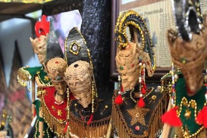 Colorful woven straw puppets with beaded outfits and tassels on display at a market stall.
