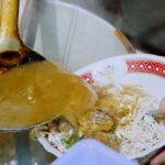 Wooden ladle scooping curry into a bowl of rice and shredded vegetables.