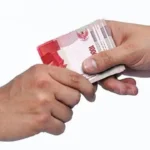 Two hands exchanging a stack of 100,000 Indonesian rupiah banknotes in a cash handoff.
