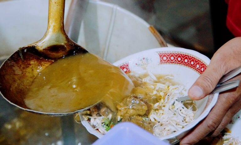 Wooden ladle scooping curry into a bowl of rice and shredded vegetables.