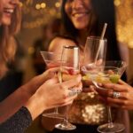 Group of friends toasting with colorful cocktails at a party, smiling and raising glasses in a celebratory moment