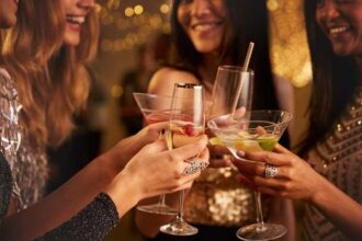 Group of friends toasting with colorful cocktails at a party, smiling and raising glasses in a celebratory moment