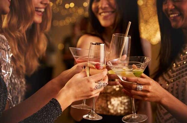 Group of friends toasting with colorful cocktails at a party, smiling and raising glasses in a celebratory moment