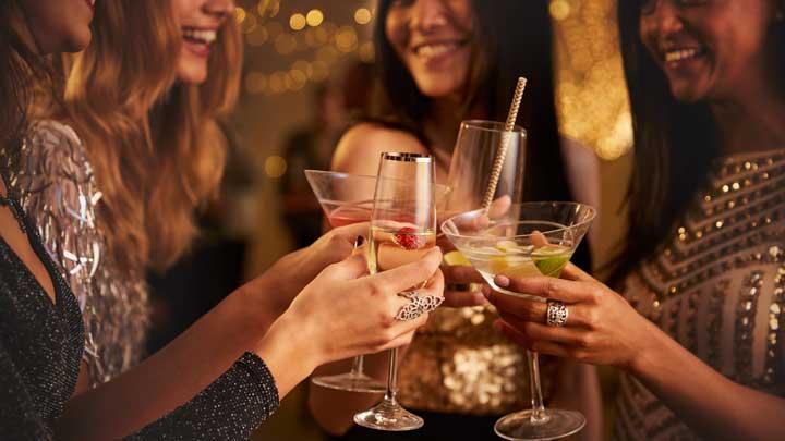 Group of friends toasting with colorful cocktails at a party, smiling and raising glasses in a celebratory moment