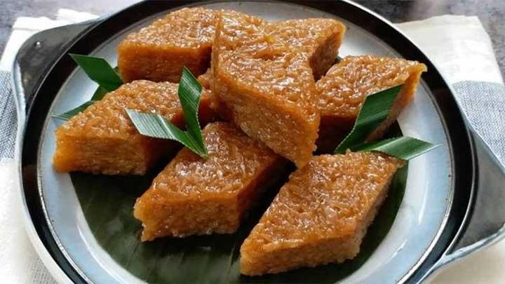 Brown rectangular jaggery-based dessert pieces arranged on a plate with green leaves as garnish, served on a dark tray