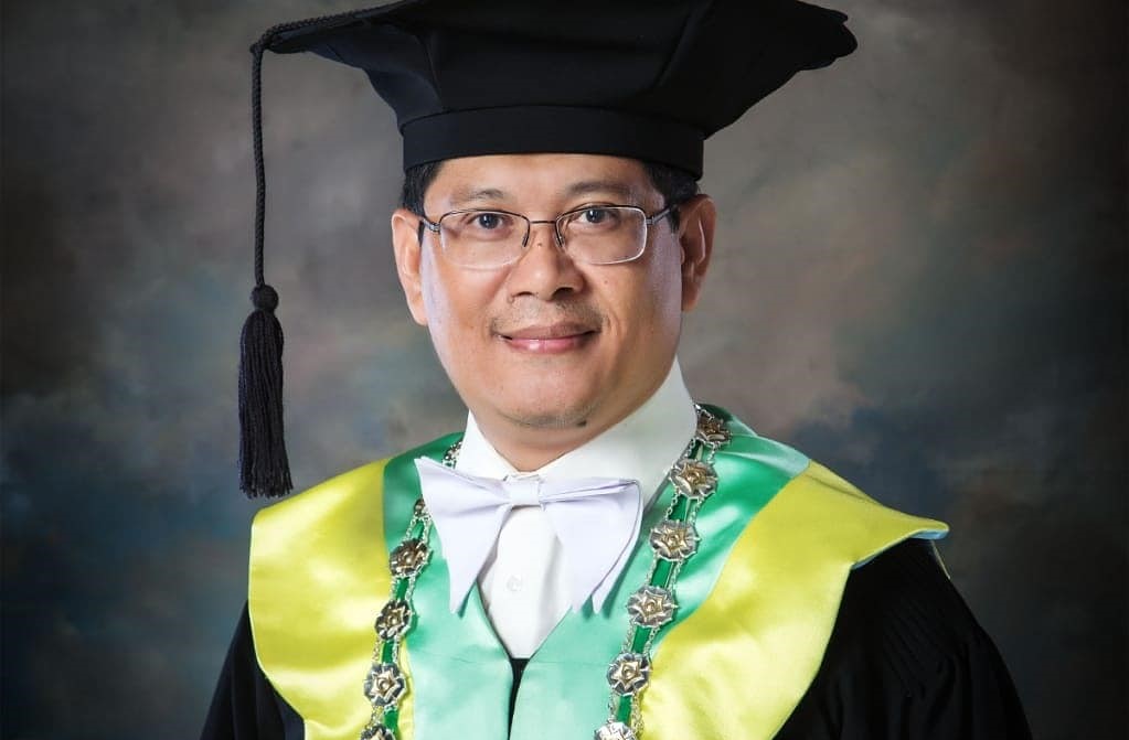111 - Mabur.co Portrait of a man in a graduation cap and gown, wearing a white bow tie and green-yellow ceremonial regalia with a silver chain and tassel.