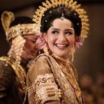 Bride in a gold embellished traditional wedding dress with an ornate headpiece, smiling at the ceremony.