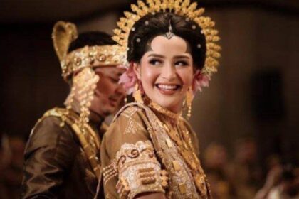 Bride in a gold embellished traditional wedding dress with an ornate headpiece, smiling at the ceremony.