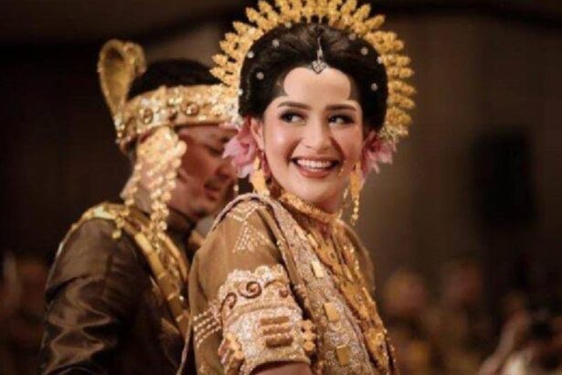 Bride in a gold embellished traditional wedding dress with an ornate headpiece, smiling at the ceremony.