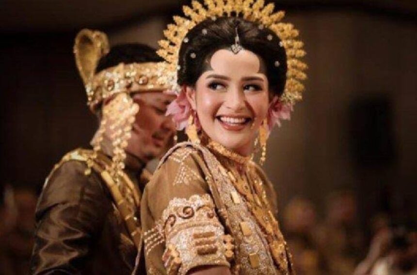 Bride in a gold embellished traditional wedding dress with an ornate headpiece, smiling at the ceremony.