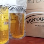 Two transparent pouches of yellow cooking oil labeled MINYAKITA beside a cardboard MINYAKITA box (Indonesian cooking oil).