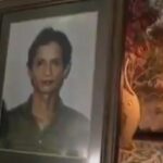 Framed portrait of a woman with short dark hair, placed on a decorative table beside a lit candle.
