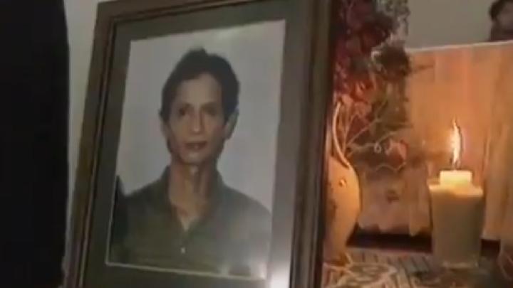 Framed portrait of a woman with short dark hair, placed on a decorative table beside a lit candle.