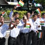 Group of Indian schoolchildren in white shirts waving small Indian flags in a parade.
