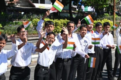 Group of Indian schoolchildren in white shirts waving small Indian flags in a parade.