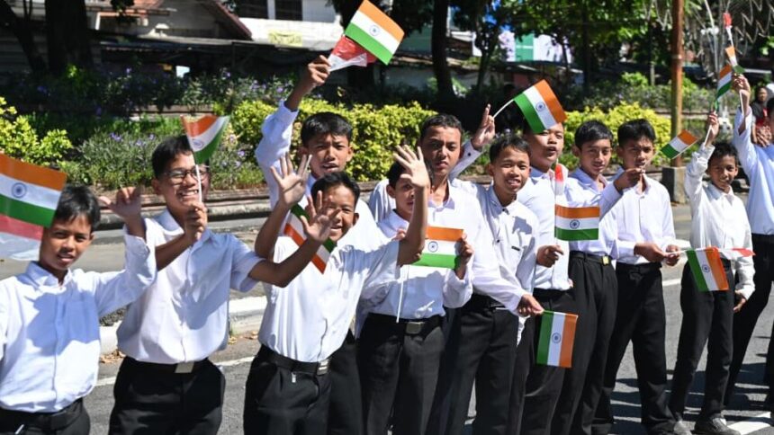Group of Indian schoolchildren in white shirts waving small Indian flags in a parade.