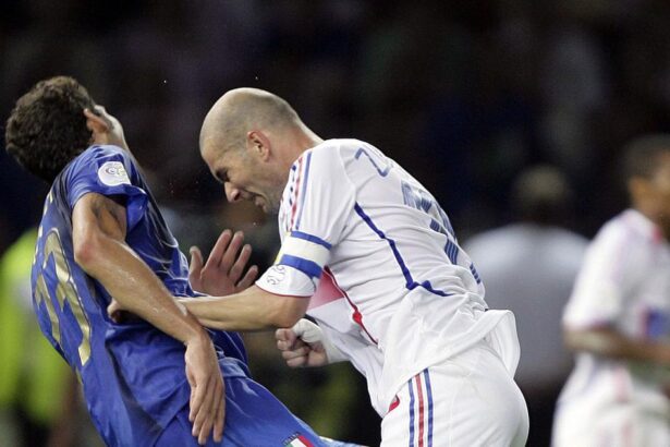 Two soccer players clash for the ball during a match: one in blue on the left and a bald man in white on the right.