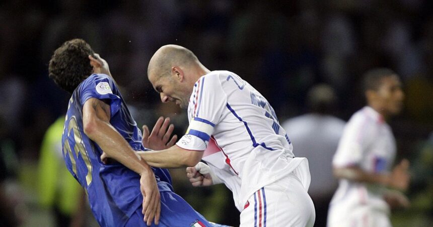 Two soccer players clash for the ball during a match: one in blue on the left and a bald man in white on the right.