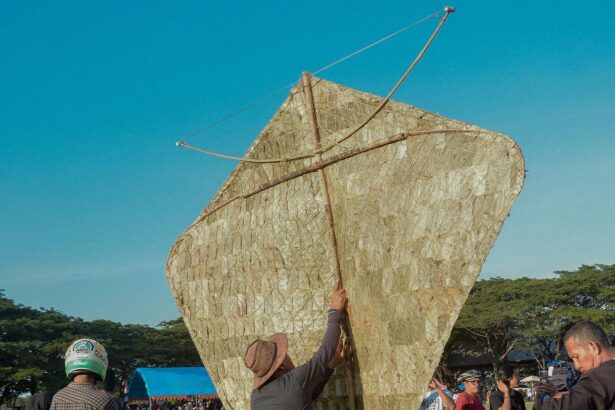 Man raises a giant triangular kite-like sail outdoors at a festival, with a crowd under a clear blue sky.