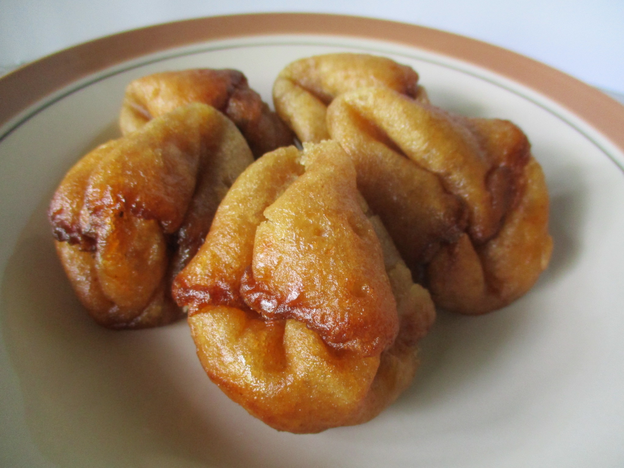 Golden brown fried dough twists on a white plate with a brown rim, crispy exterior.