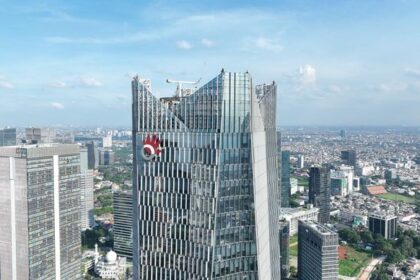 Aerial view of a modern city skyline with glass skyscrapers, including a tall building under construction with cranes.