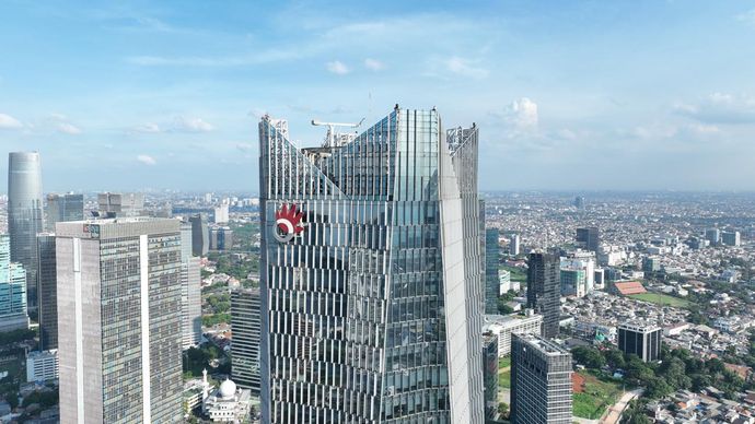 Aerial view of a modern city skyline with glass skyscrapers, including a tall building under construction with cranes.