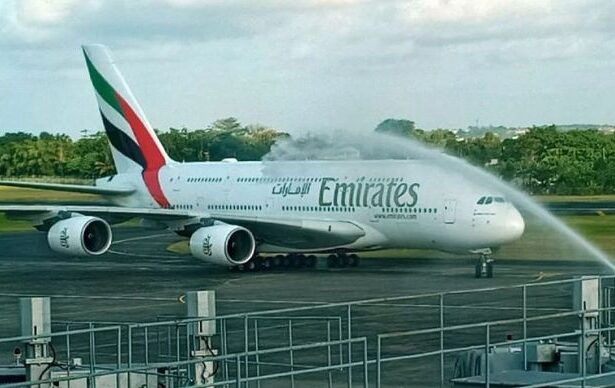 Emirates Airbus A380 on the tarmac receiving a water salute from airport fire trucks."