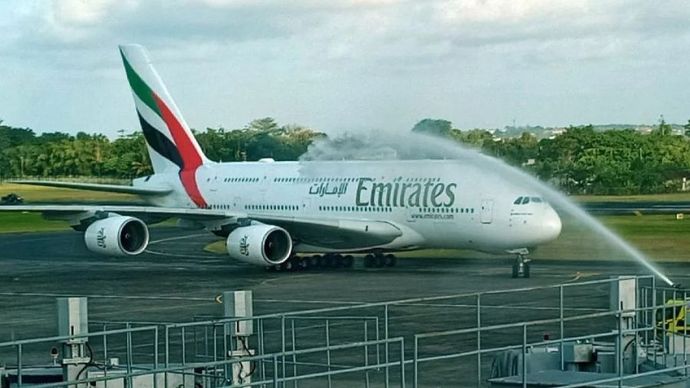 Emirates Airbus A380 on the tarmac receiving a water salute from airport fire trucks."