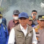Group of Indonesian officials and police in uniform, outdoors, with smoke in the background, speaking to media or briefing.