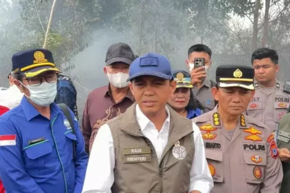 Group of Indonesian officials and police in uniform, outdoors, with smoke in the background, speaking to media or briefing.