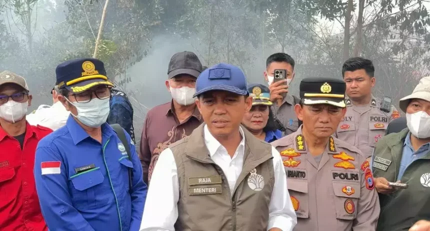 Group of Indonesian officials and police in uniform, outdoors, with smoke in the background, speaking to media or briefing.