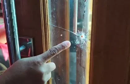 A hand points at a spider crack in the glass panel of a wooden door, highlighting the damage.