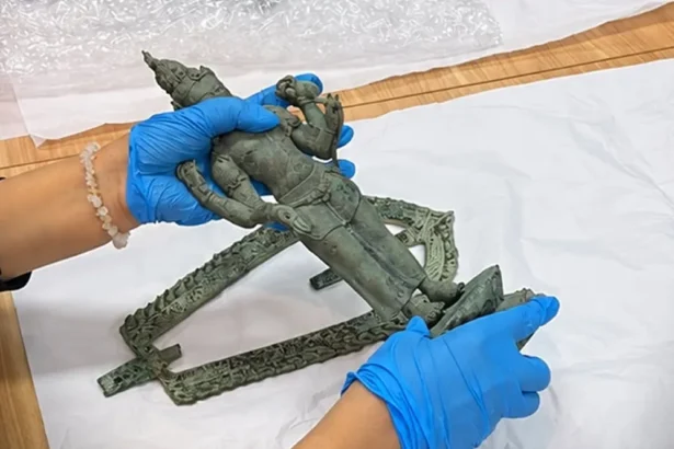 Gloved hands join pieces of a green bronze statue on a white work surface during restoration.