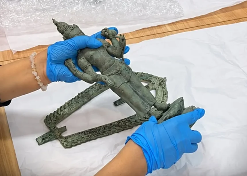 Gloved hands join pieces of a green bronze statue on a white work surface during restoration.