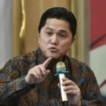 Man in a brown batik shirt speaks into a gold handheld microphone, gesturing with his index finger as he makes a point during a discussion.