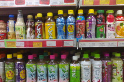 Row of colorful bottled drinks on supermarket shelf, with yellow, blue, and green caps and various fruit-tea and juice labels.