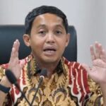 Man wearing a batik shirt speaks into a microphone with hands raised for emphasis.
