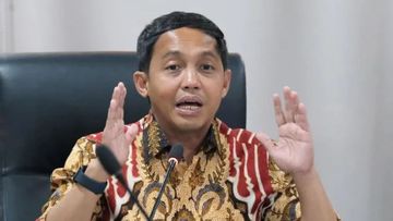 Man wearing a batik shirt speaks into a microphone with hands raised for emphasis.