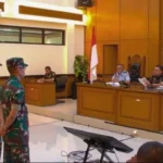 Soldiers in camouflage stand before a panel of officials in a wood-paneled courtroom, Indonesian flag visible.