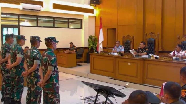 Soldiers in camouflage stand before a panel of officials in a wood-paneled courtroom, Indonesian flag visible.