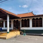 Front view of a white building with orange tiled roof, arched windows, and a yellow-tiled entrance stairs leading to a porch.